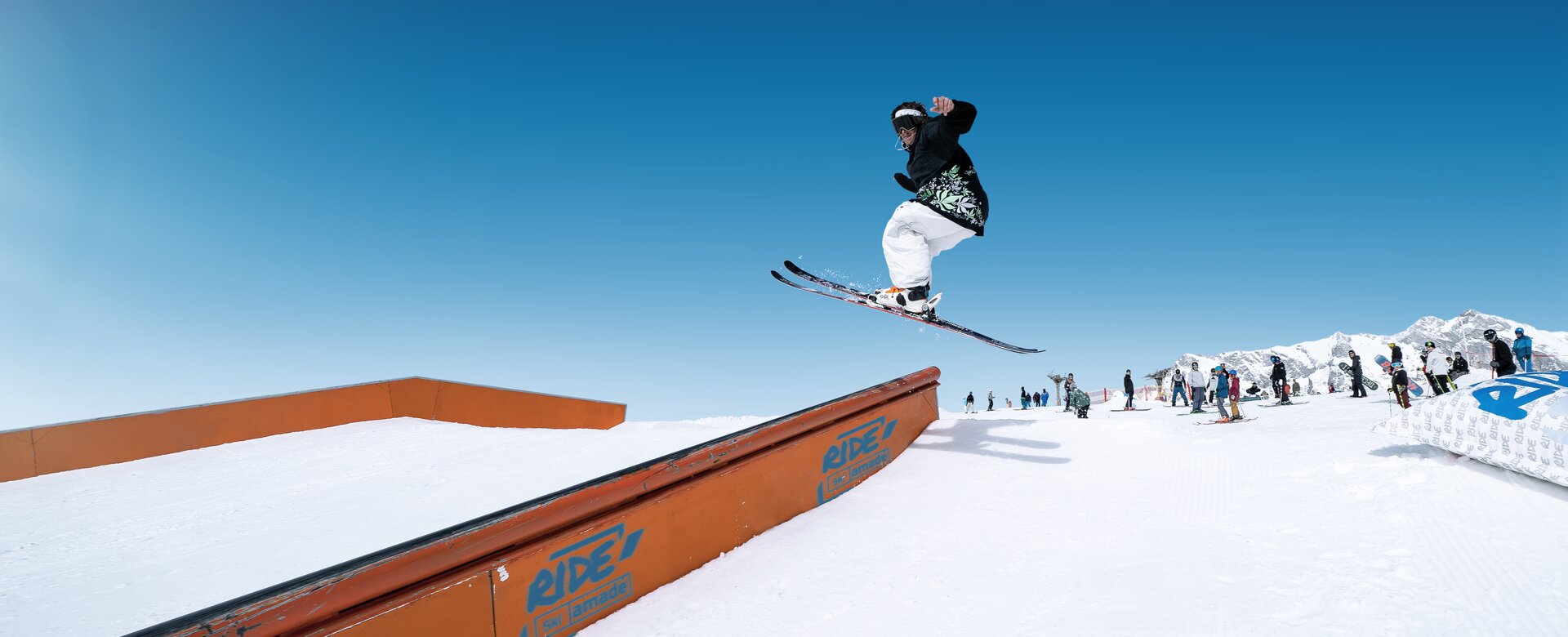 Freestyler springt mit quergestellten Ski auf eine Metallvorrichtung auf der man hinunter gleiten kann