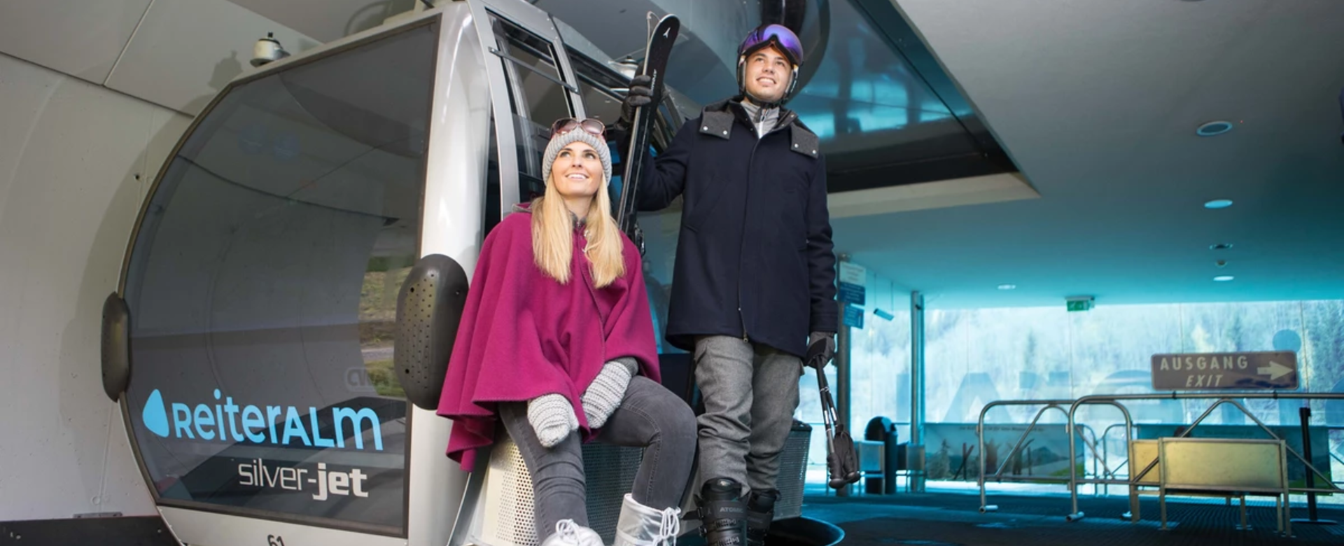 A female and a male model pose in front of a Reiteralm gondola in new winter fashion. | © Reiteralm Bergbahnen
