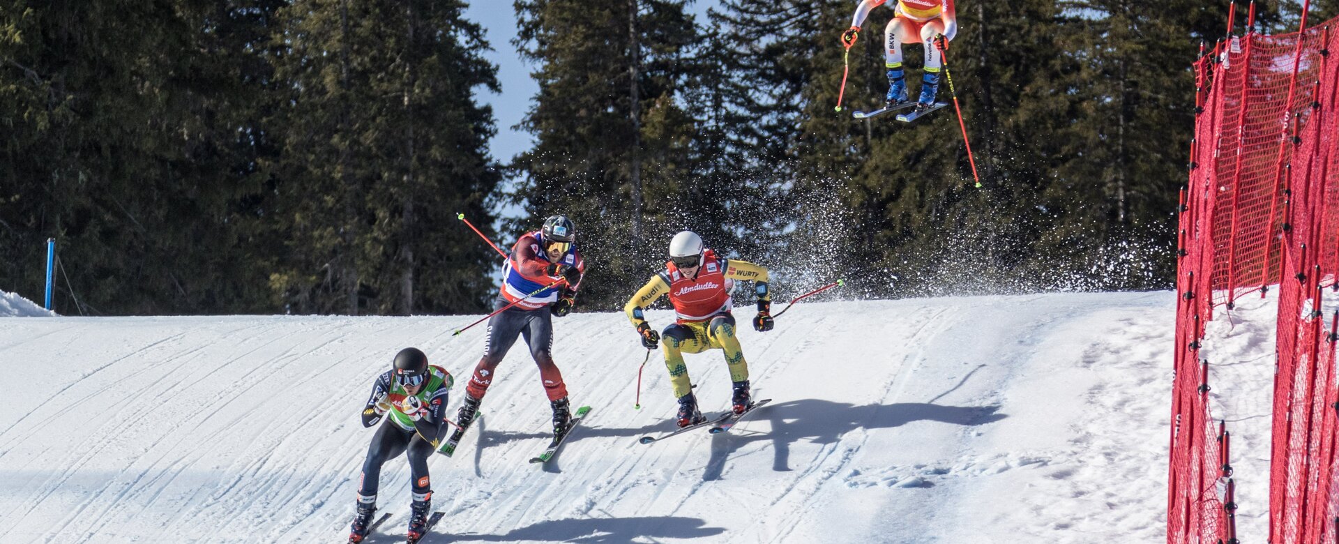 Vier Skicross Läufer fahren gerade den Lauf herunter. Drei Rennläufer fahren auf der Piste während ein Läufer noch über einen Hügel springt. | © Reiteralm Bergbahnen/Gerald.Grünwald