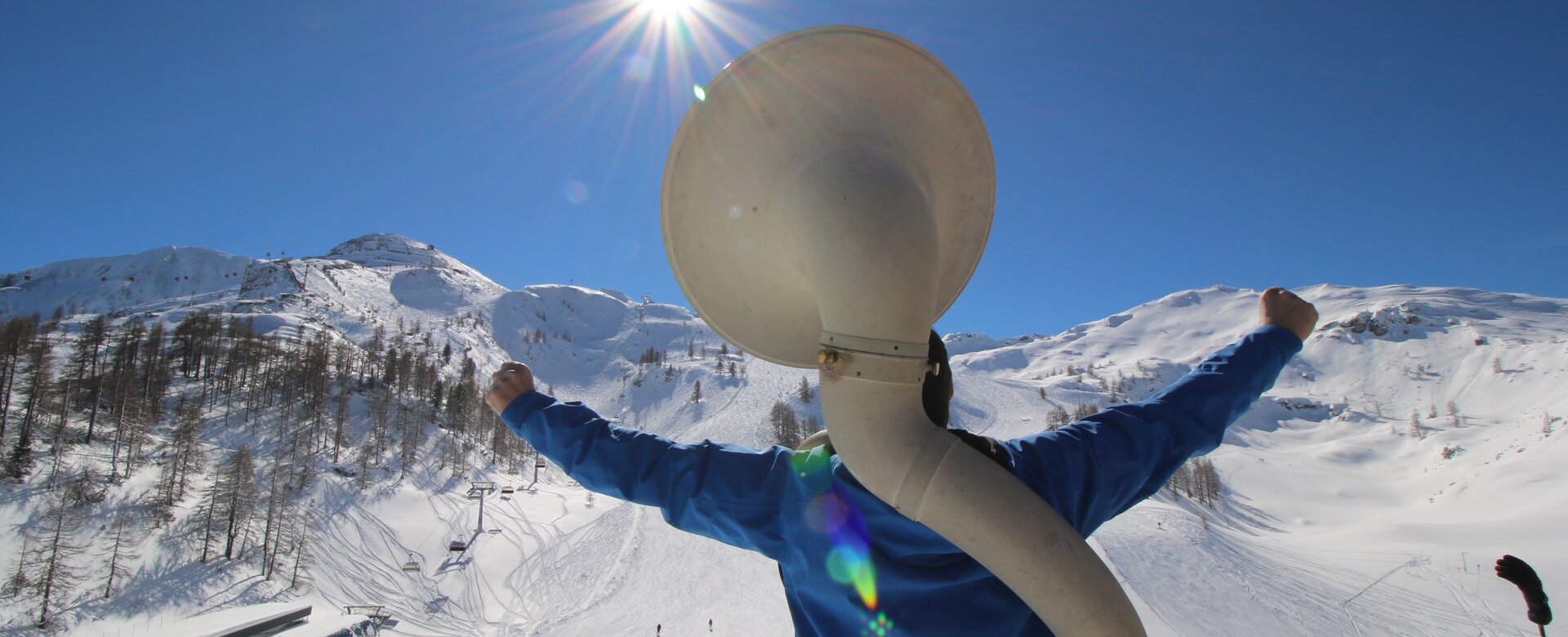 Person with a blue jumper stands in front of the ski slope and a white wind instrument can be seen on the back | © Liftgesellschaft Zauchensee