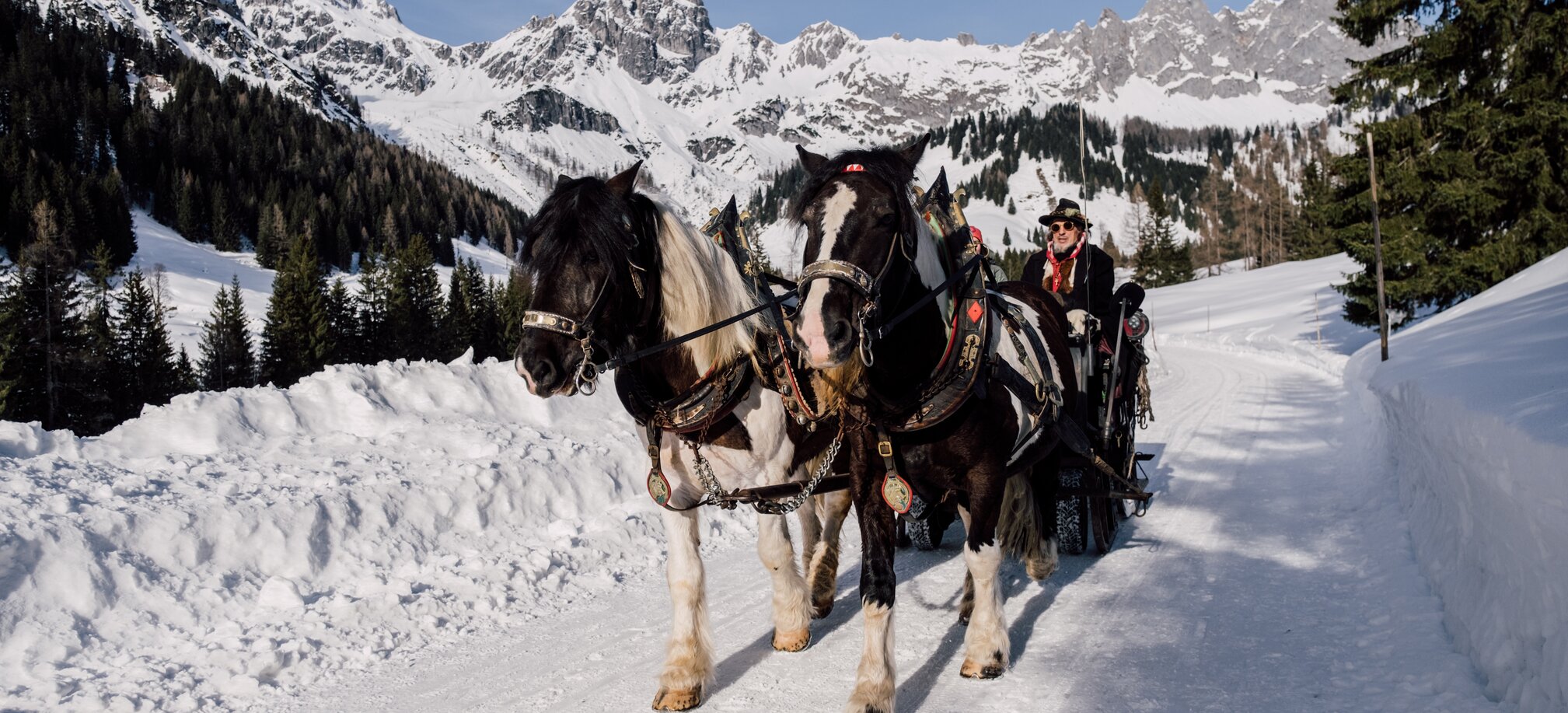 A horse-drawn sleigh with two horses glides through the snowy mountain landscape. | © Chris Perkles