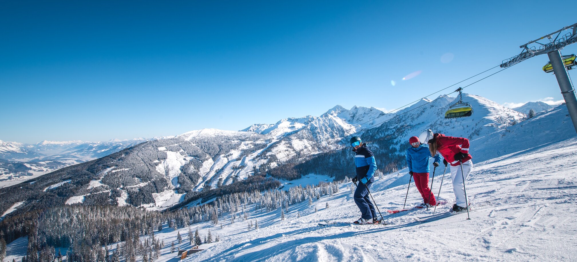 Three skiers stand on a slope overlooking snow-covered mountains. | © Ski amadé